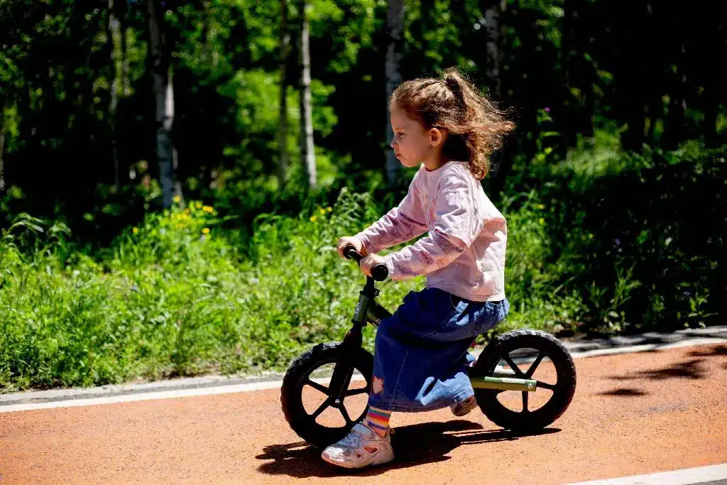 Child riding a balance bike on a sunny path in a lush green park