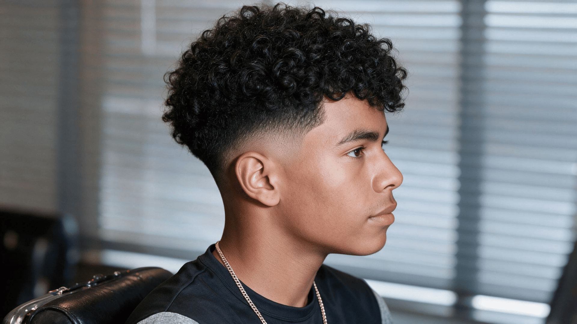 black man with defined curls on top and a smooth mid fade around the sides and temples