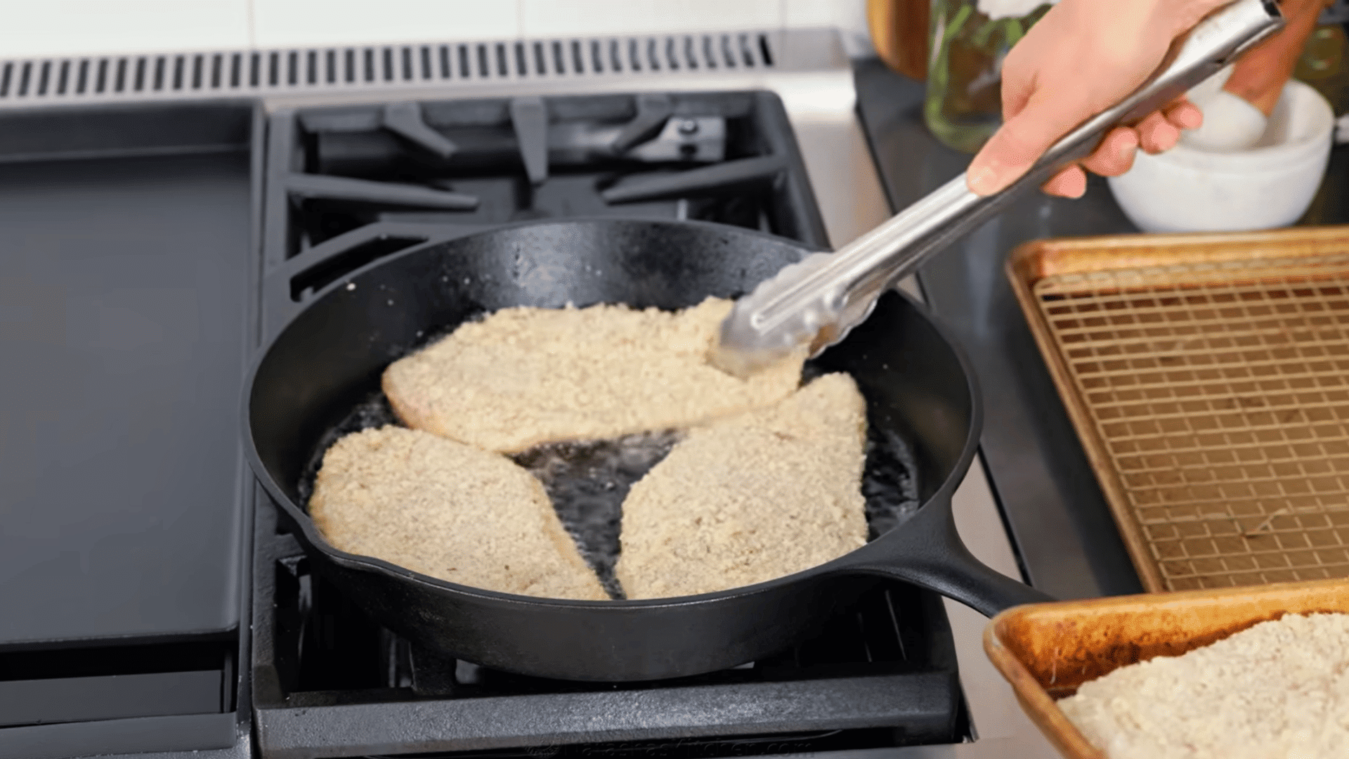 breaded chicken cutlets pan frying in hot oil in a cast iron skillet.