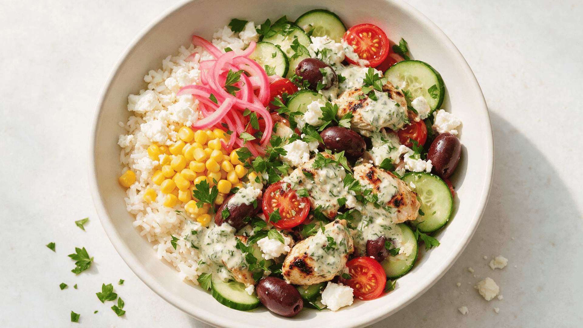 cava-style chicken bowl with rice, grilled chicken, cucumbers, tomatoes, corn, feta, olives, pickled onions, and creamy herb dressing.