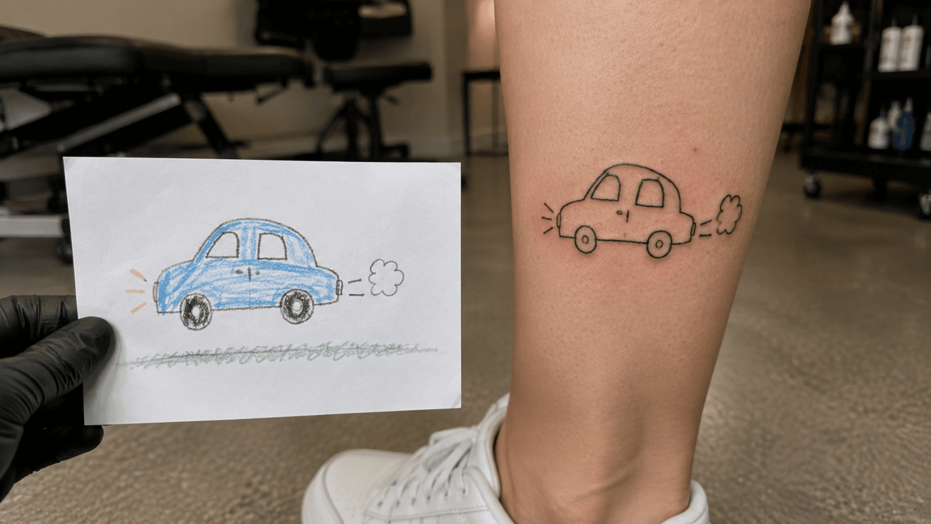 child’s blue car drawing beside a matching small car tattoo on the lower leg
