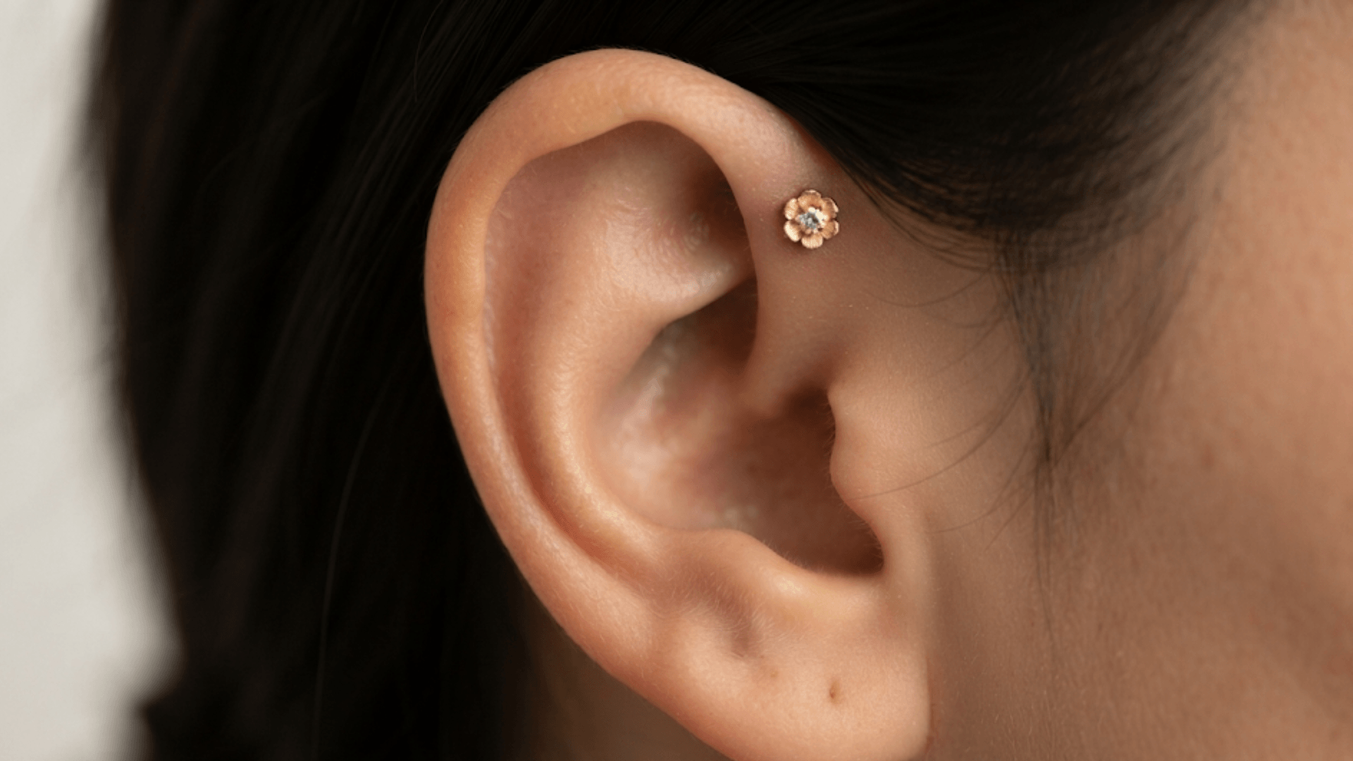 close up ear with a delicate floral forward helix stud piercing near the upper front cartilage