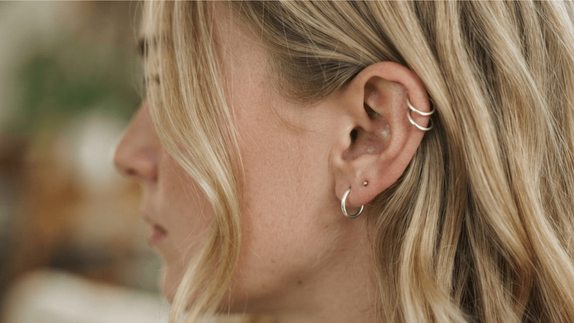 close up of double helix piercing with silver hoops and small lobe earrings on a blonde woman