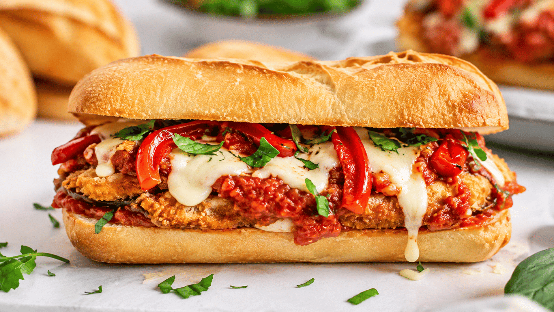 closeup sandwich on crusty bread filled with breaded eggplant tomato sauce melted cheese roasted peppers and fresh parsley on parchment