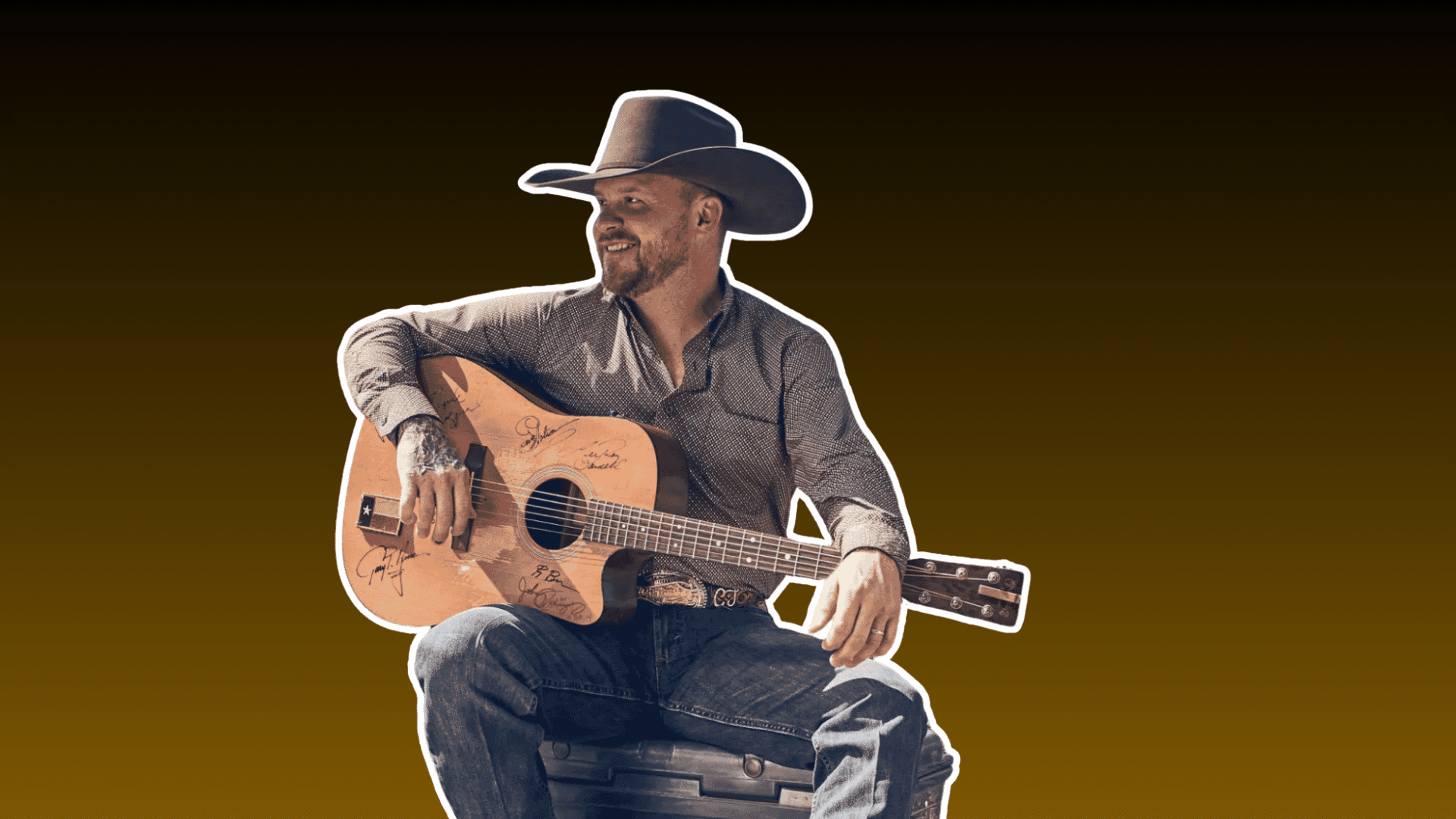 country musician wearing a cowboy hat seated with an acoustic guitar against a dark brown background
