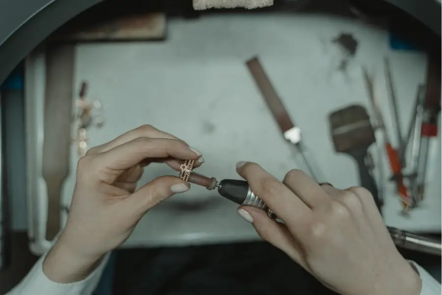 Hands polishing a gold ring with a rotary tool at a jeweler's workbench