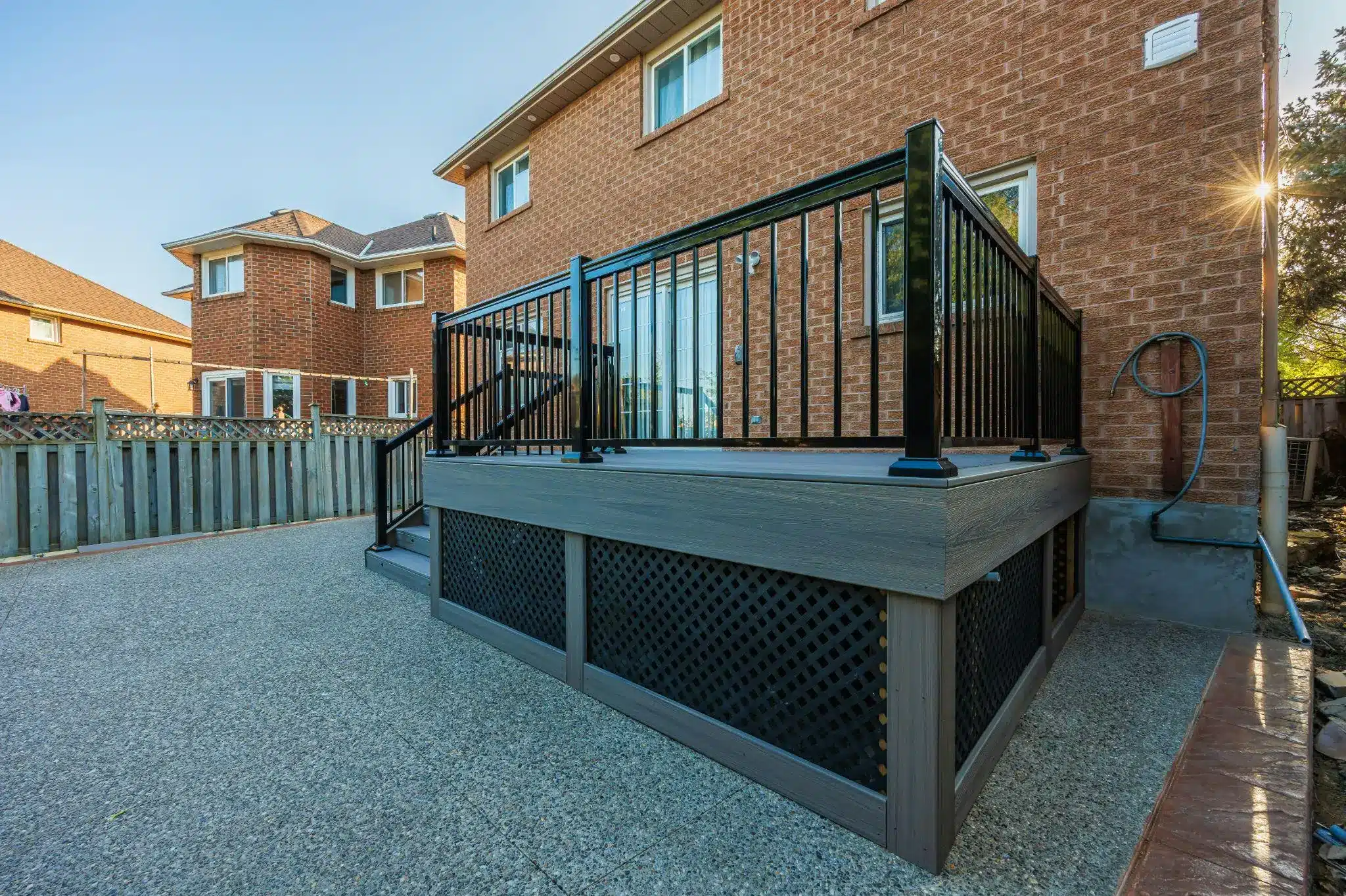 Elevated deck with black metal railing beside brick house in sunny backyard setting
