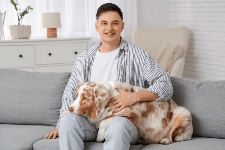 Man sitting on gray sofa with a dog in bright living room