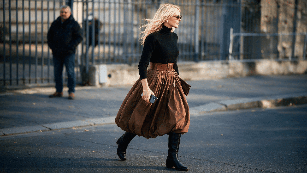 fall boho chic outfit with a brown flowing skirt, black turtleneck, wide leather belt, knee-high boots, and simple accessories