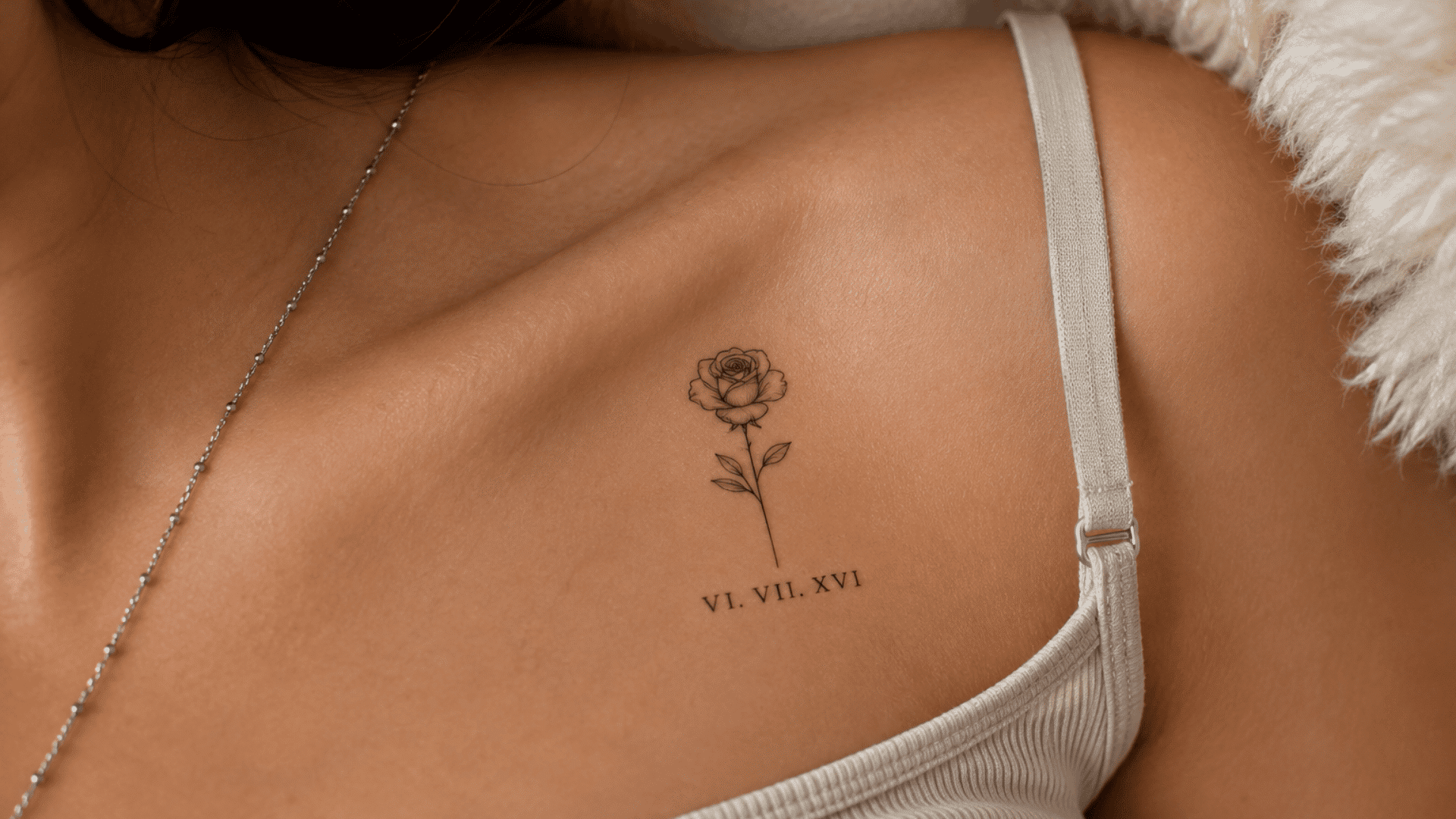 fine-line rose tattoo with Roman numerals VI. VII. XVI. below it on the collarbone.