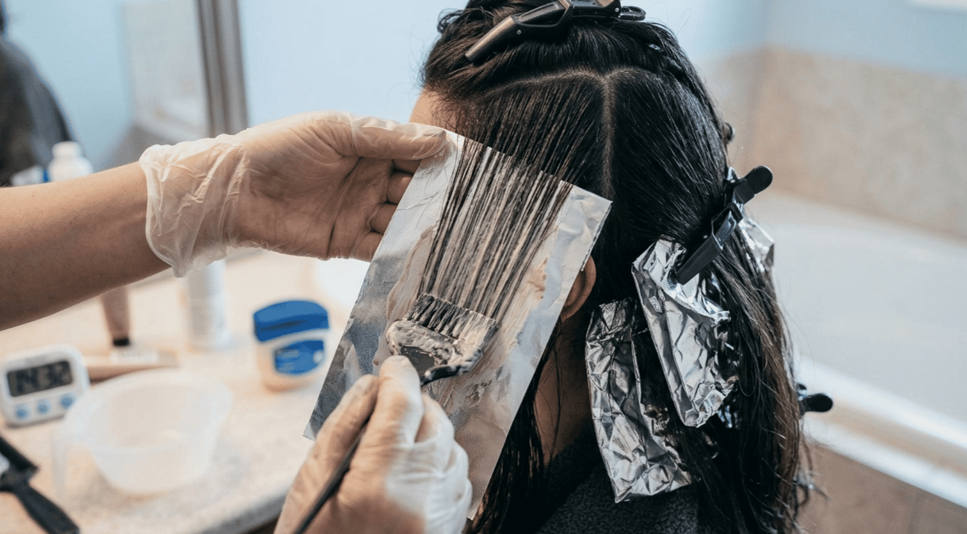 hair colorist applying lightener to sectioned dark hair with foil during a highlighting treatment