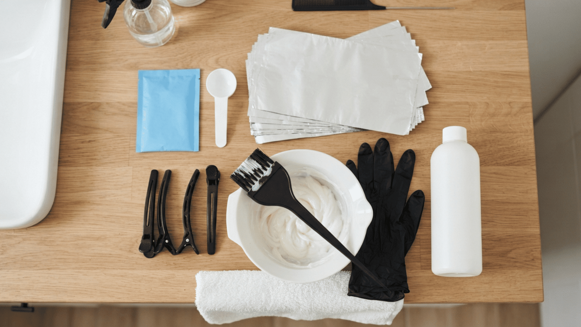 Hair lightening kit with developer, gloves, brush, clips, bowl, and foil arranged on a surface.