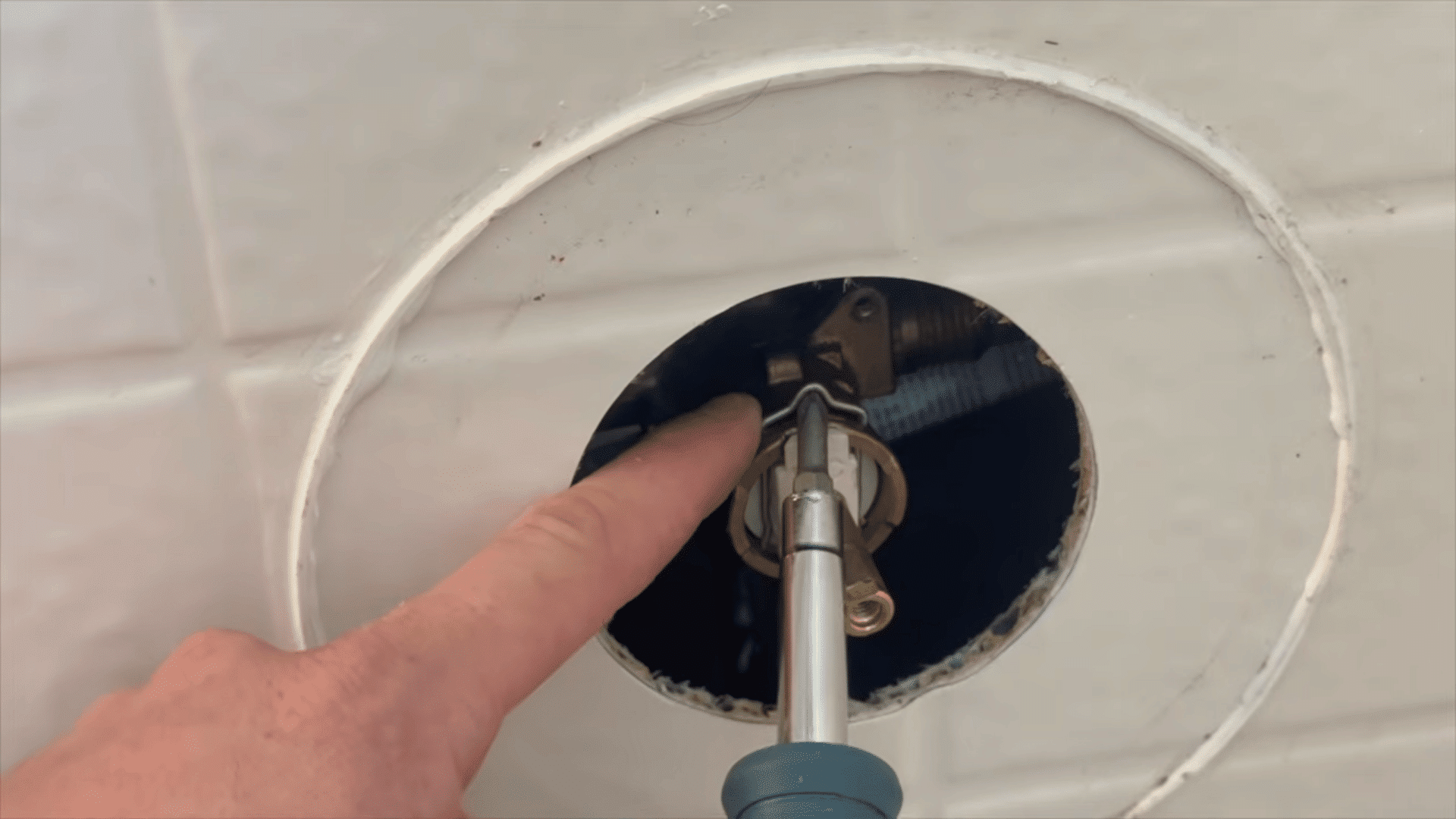 hand pointing at screwdriver prying metal retaining clip off shower cartridge