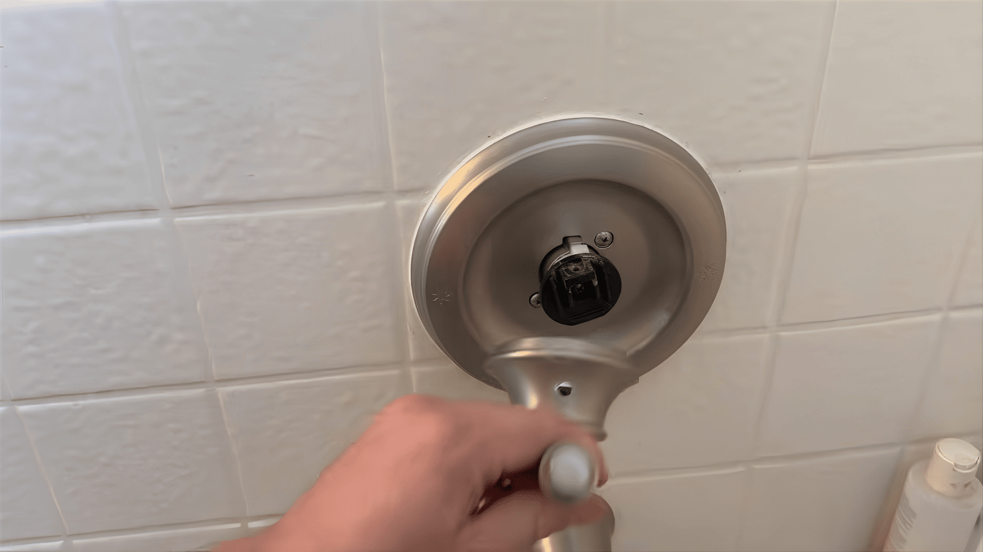 hand removing brushed nickel shower handle from wall valve assembly