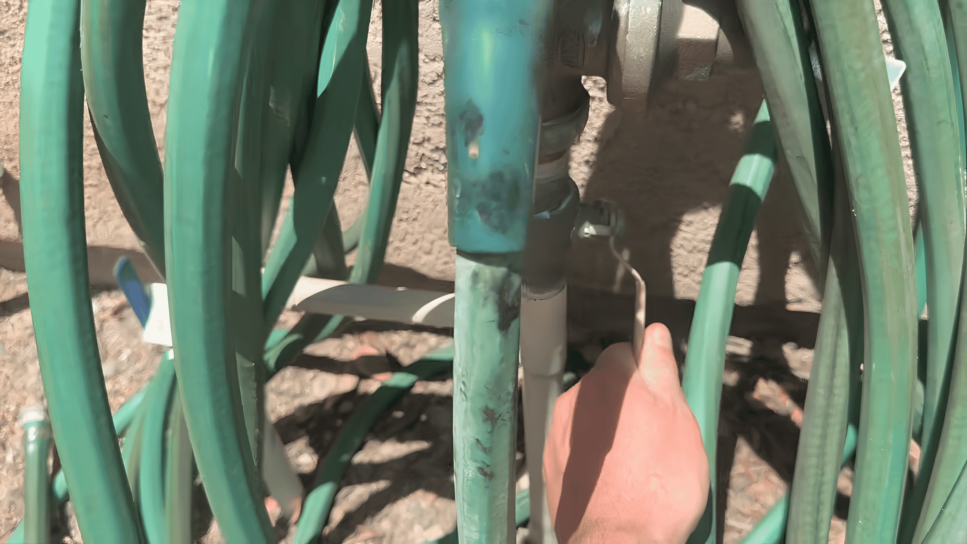 hand turning outdoor main water shut off valve near green garden hose