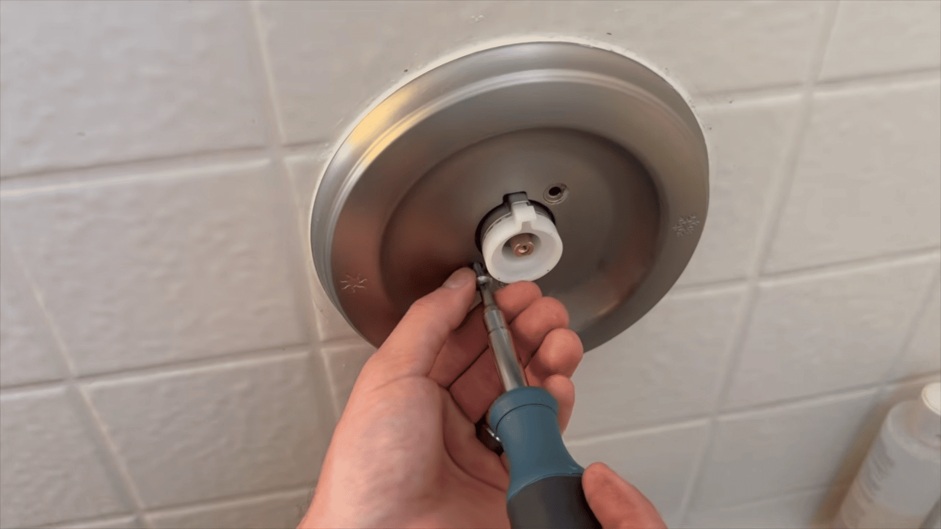 hand using screwdriver to attach metal shower faceplate back to wall.