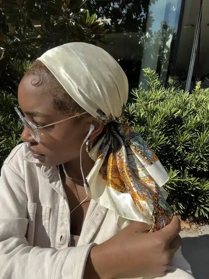 Woman with patterned headscarf and glasses sitting outdoors under natural light