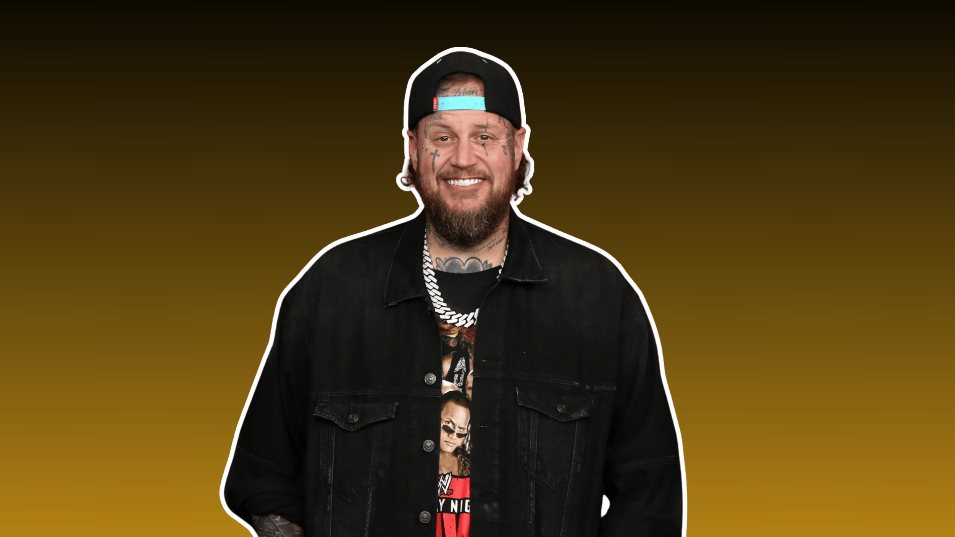 jelly roll smiling in a black jacket and backward cap against a warm brown background