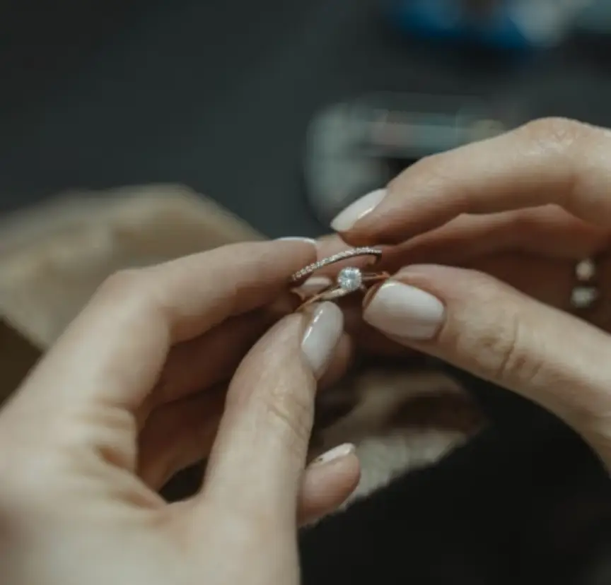 Hands holding diamond engagement ring with delicate band in softly lit room