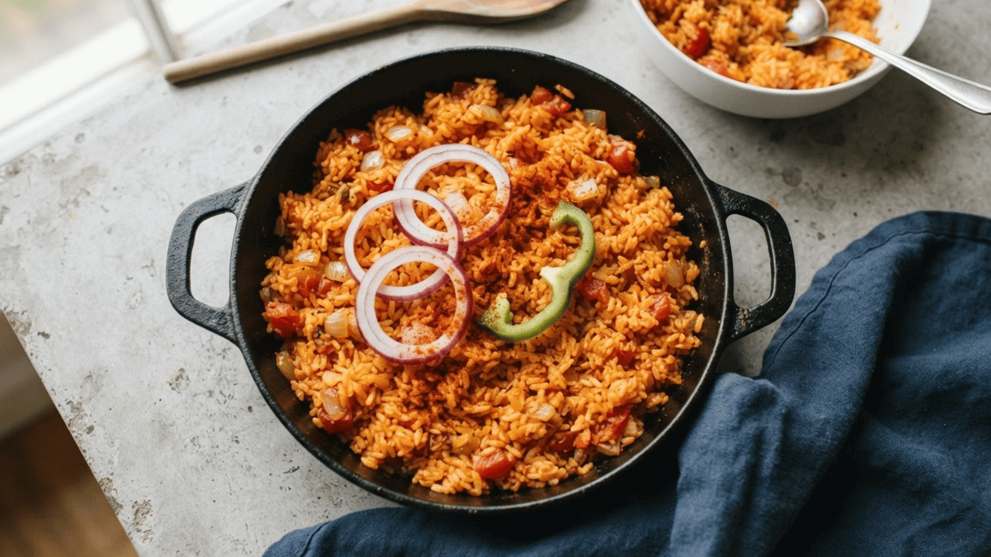 jollof rice served in a black pan with onions and peppers on top