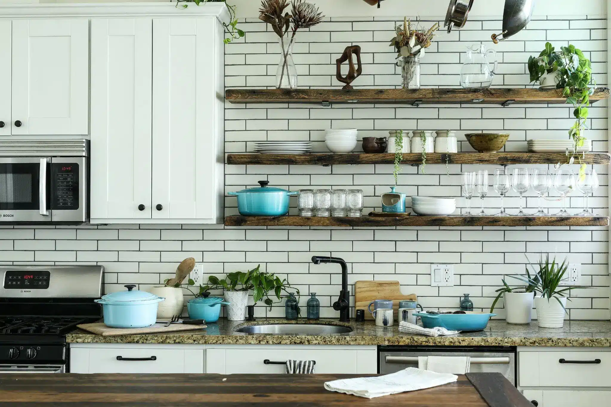 Rustic kitchen with white subway tiles, wooden shelves, blue pots, and potted plants on granite counter