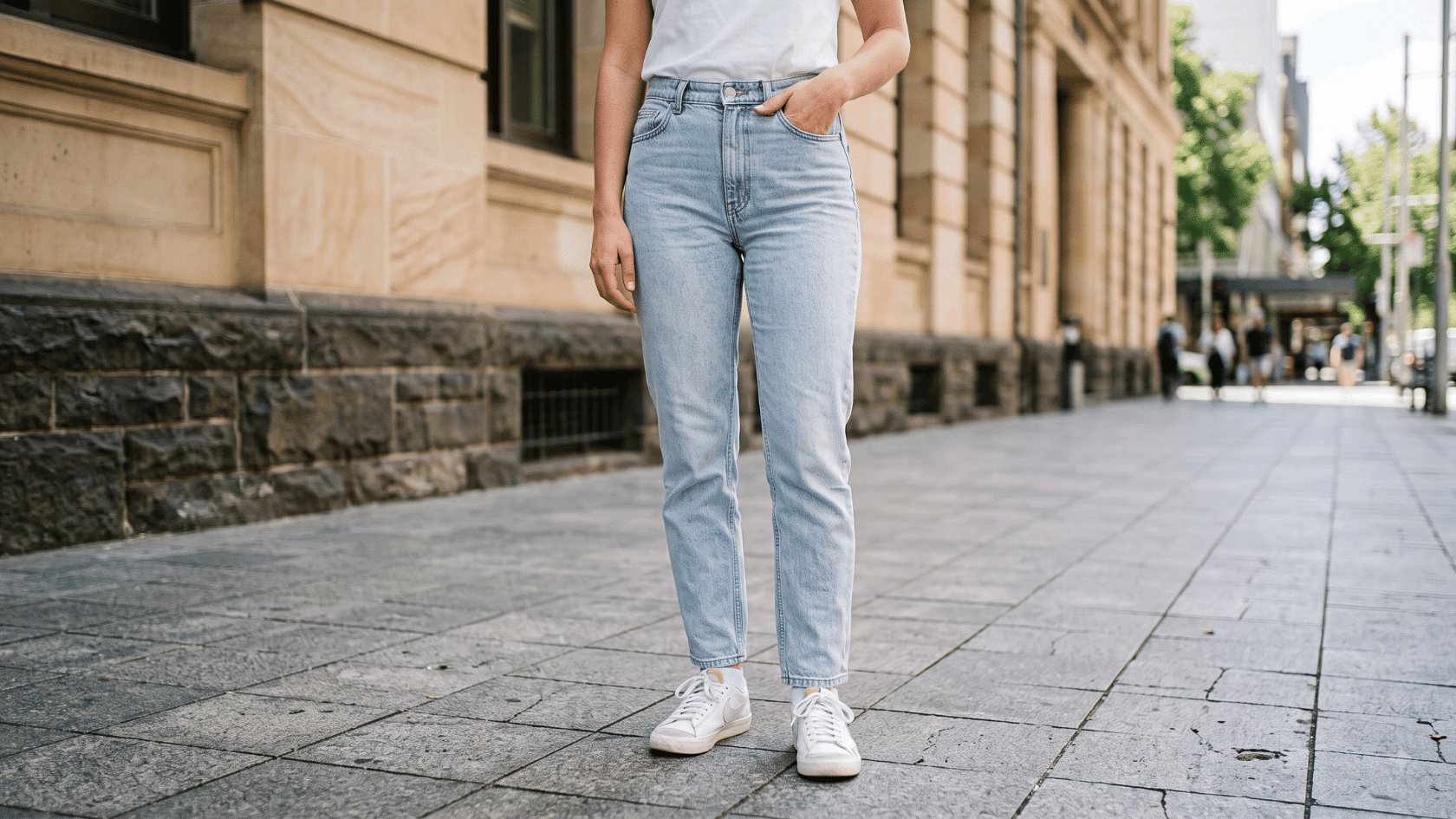 Light-wash mom jeans paired with a white top and sneakers on a city sidewalk.