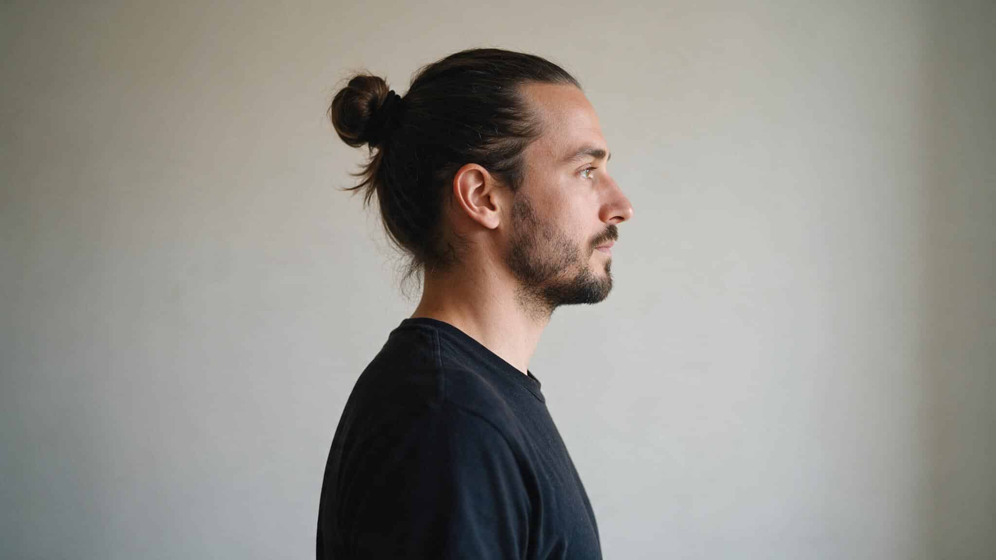 long black hair styled into a high man bun with loose face framing strands creating a relaxed hairstyle for men