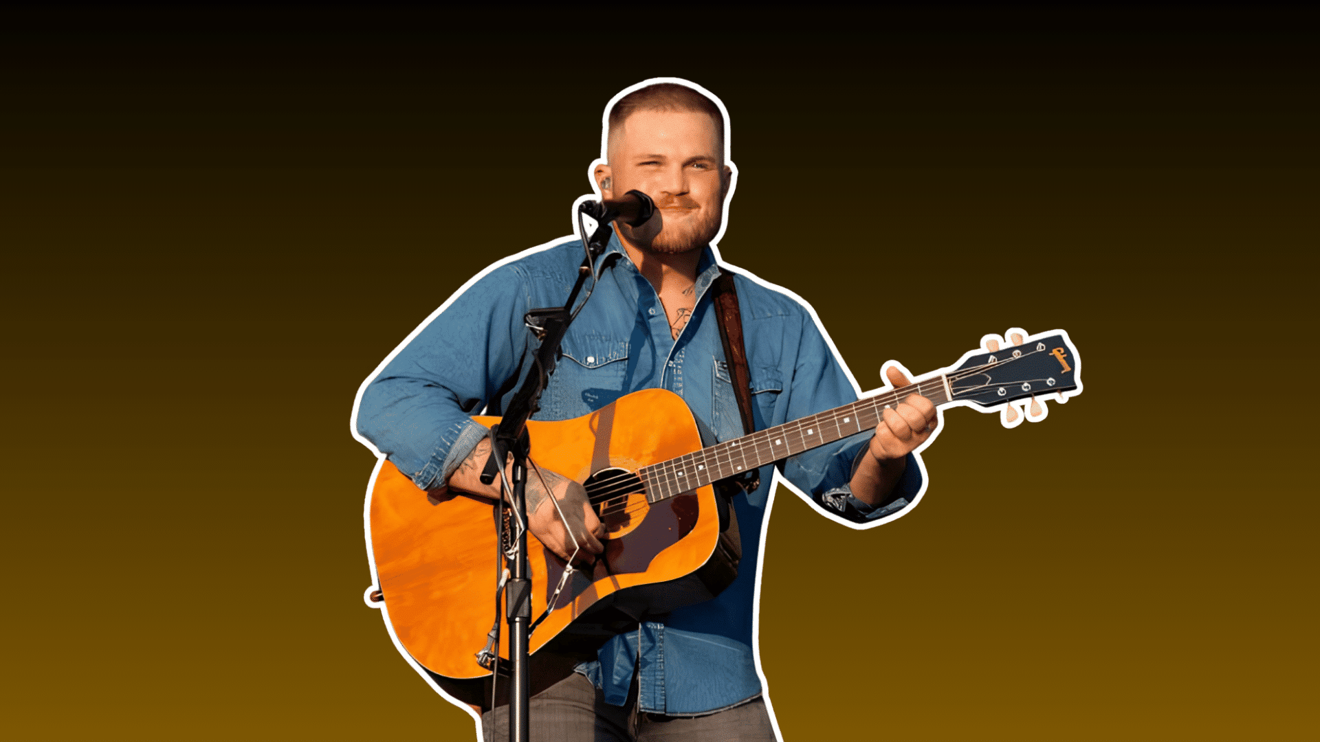 male country musician playing acoustic guitar and singing into a microphone while wearing a blue denim shirt