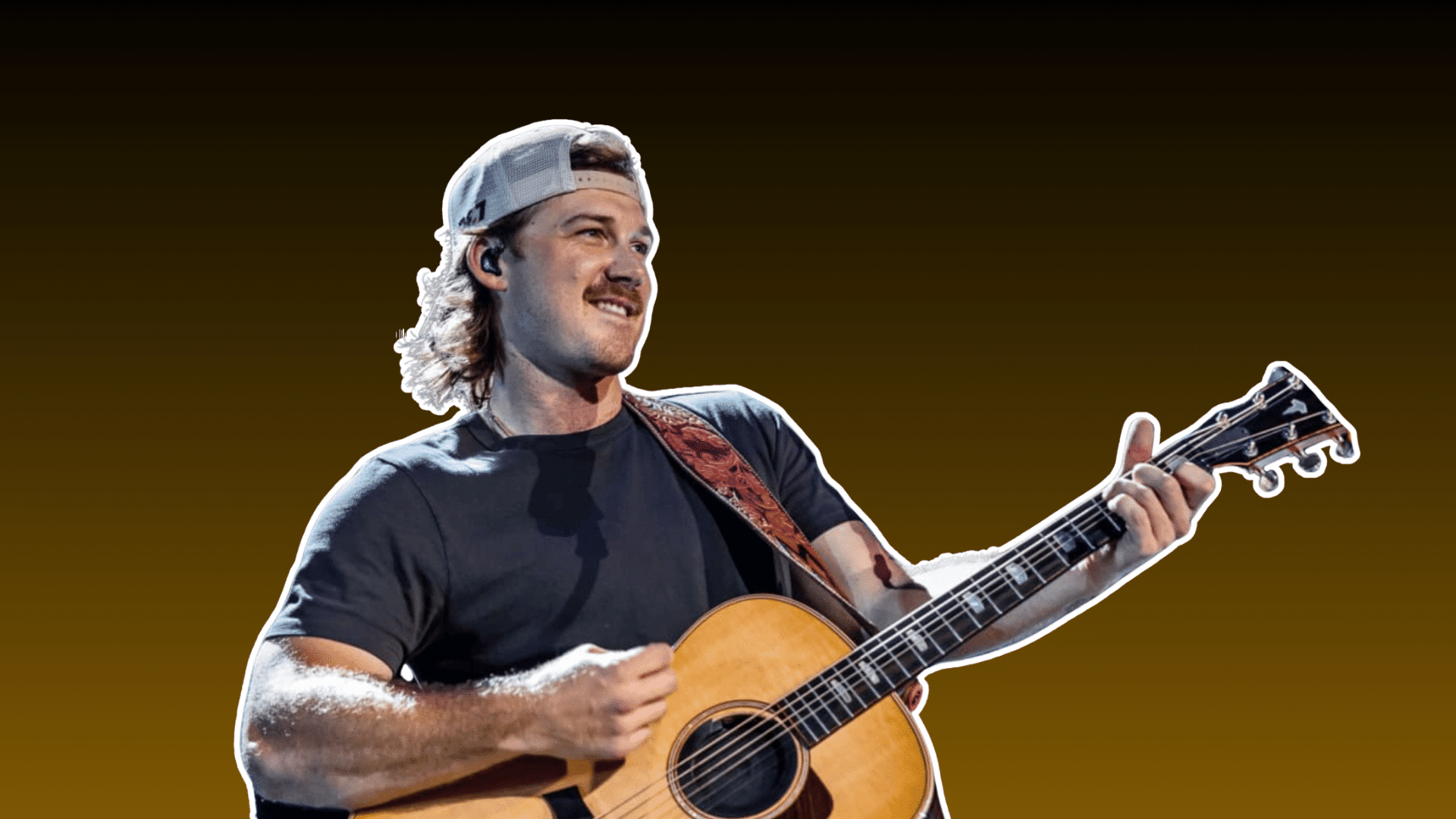 male country musician wearing a backward cap and dark shirt smiling while playing an acoustic guitar