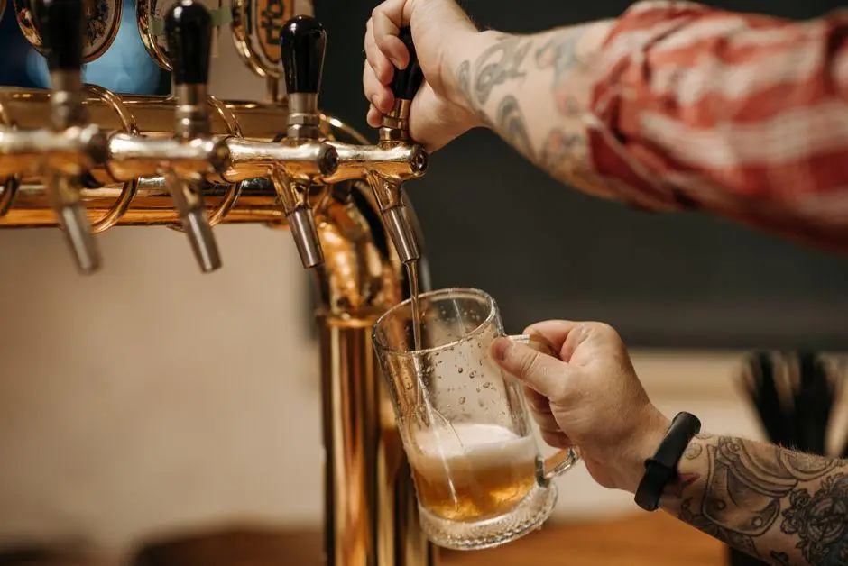 Tattooed bartender pouring beer into glass mug from brass taps in a bar setting
