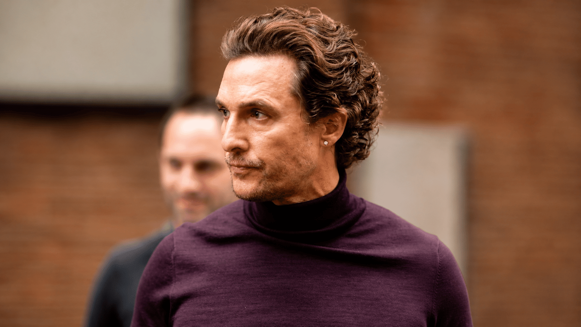 man wearing a bro flow haircut with wavy medium length hair light stubble and dark purple turtleneck sweater