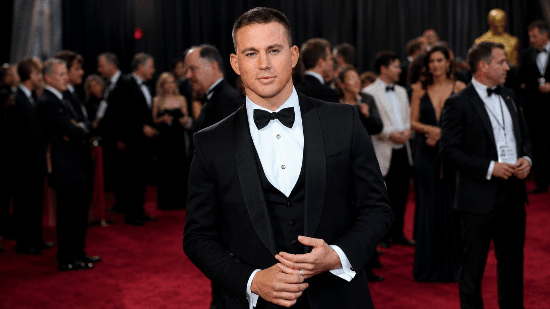 man wearing a crew cut with black tuxedo white shirt vest and bow tie while posing on a formal red carpet