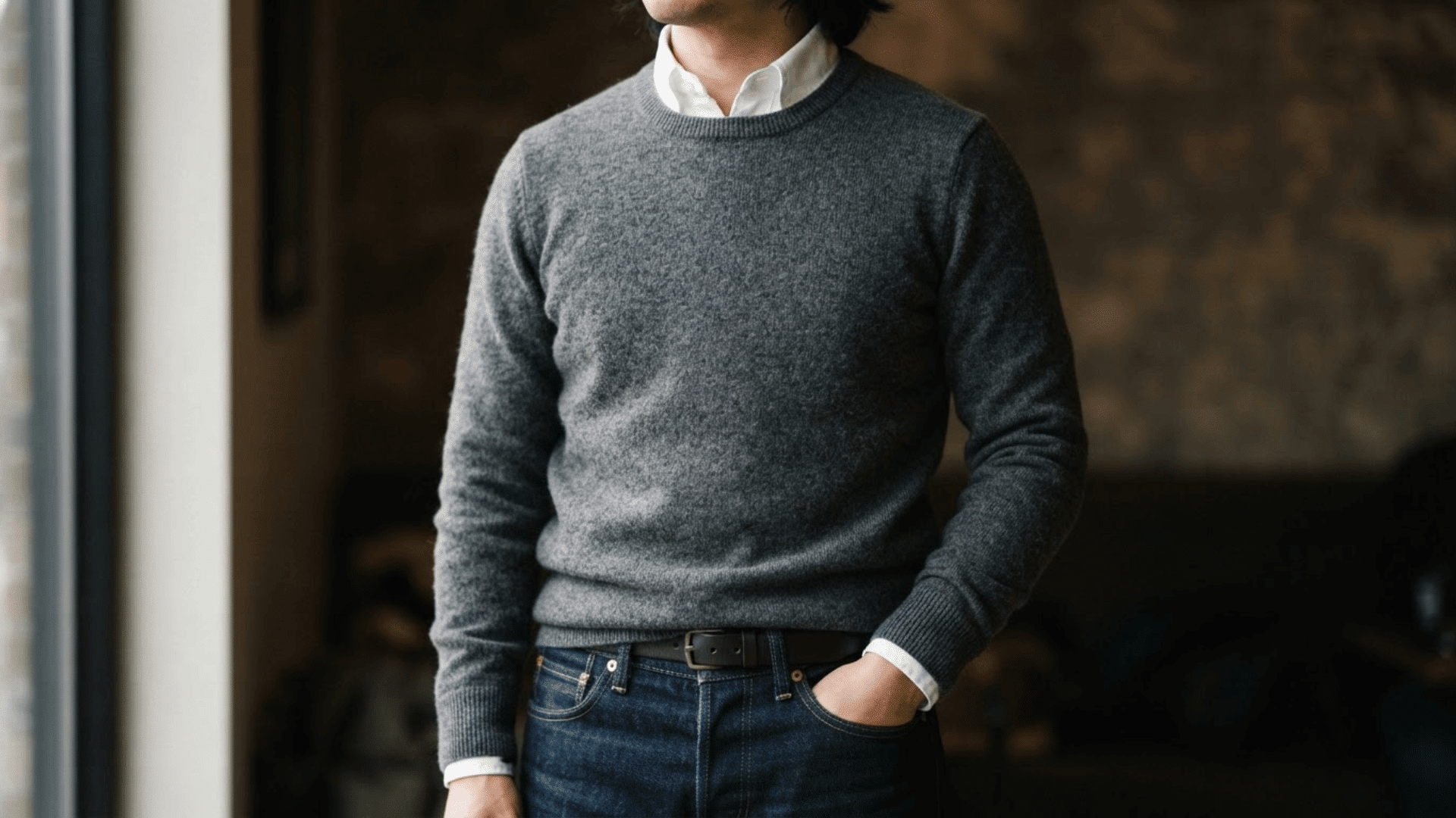 man wearing a neutral sweater over a collared shirt with dark jeans