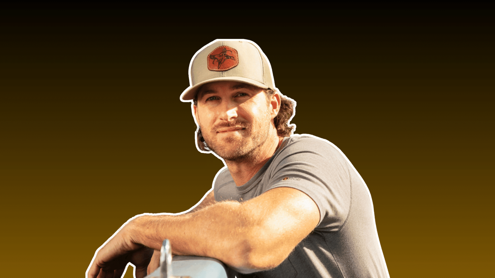 man wearing a tan cap and gray shirt posing casually against a dark brown background