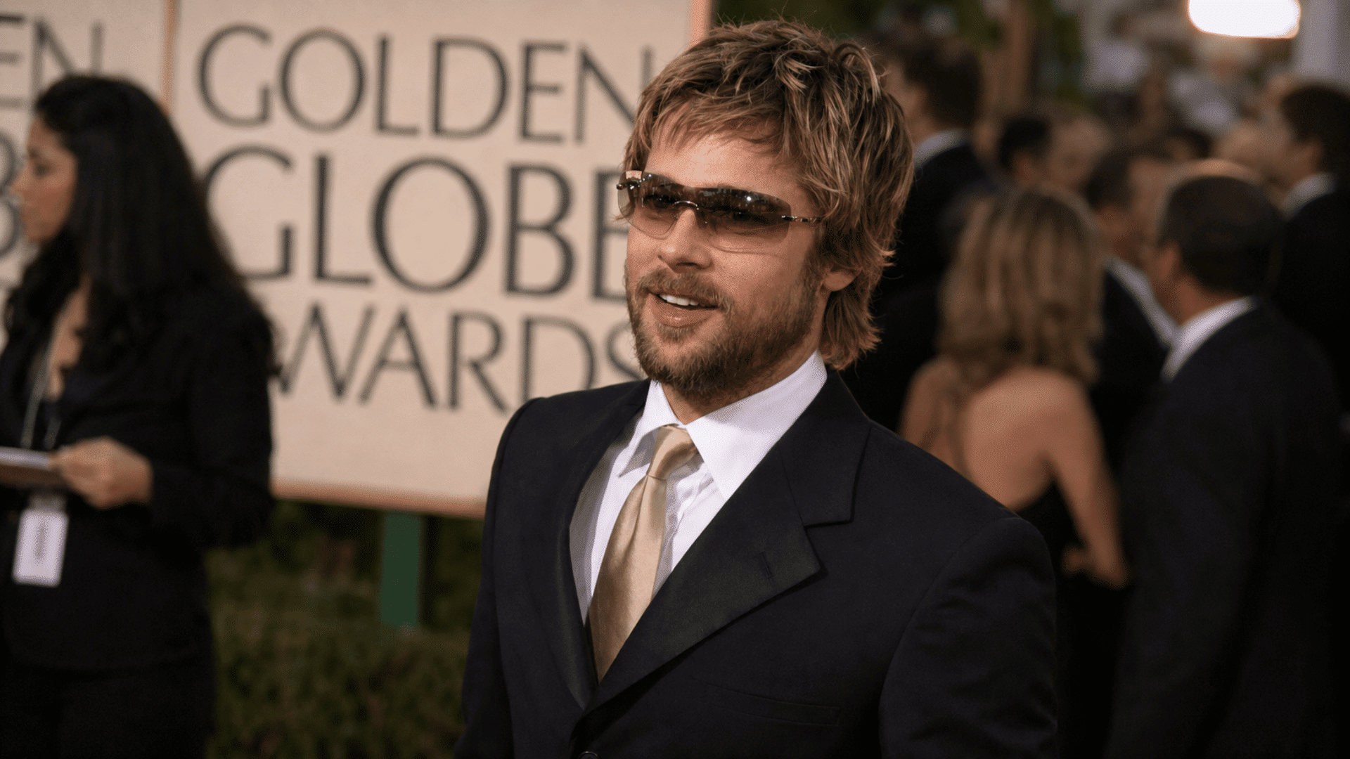 man wearing shaggy layered hair with beard sunglasses dark suit white shirt and gold tie at a formal event