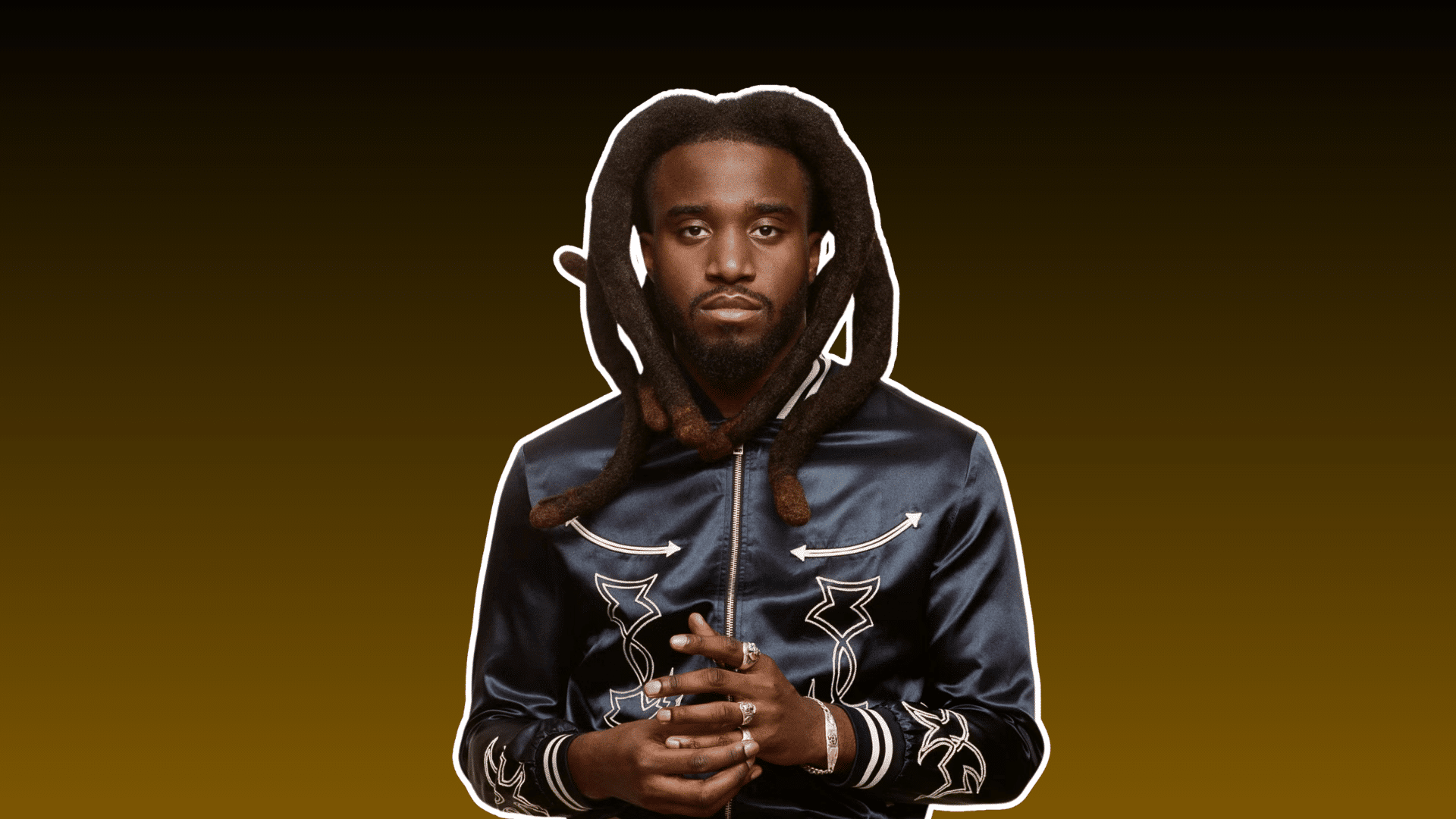 man with long dreadlocks wearing a dark embroidered jacket and rings against a brown background