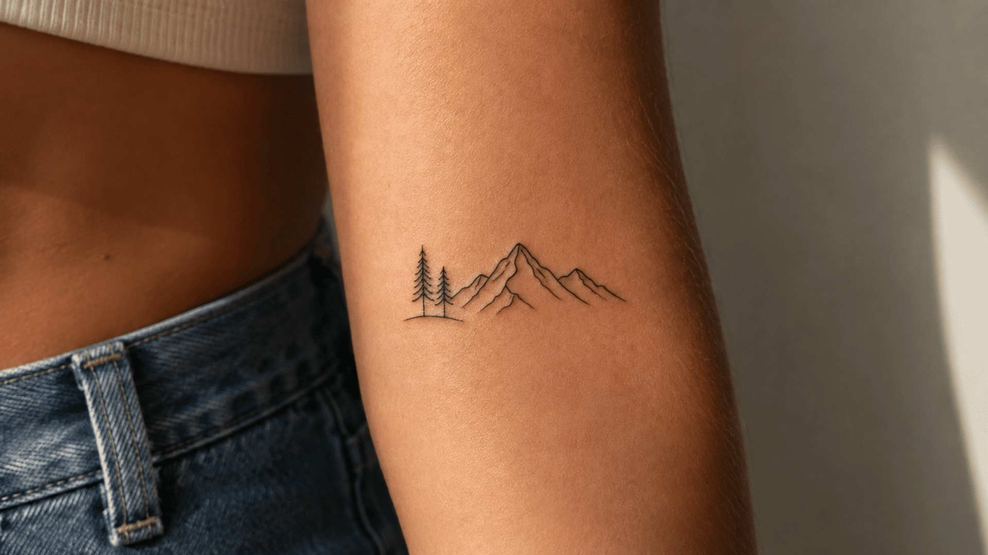 minimalist mountain range tattoo with two pine trees and a small wave in fine black lines on the arm.