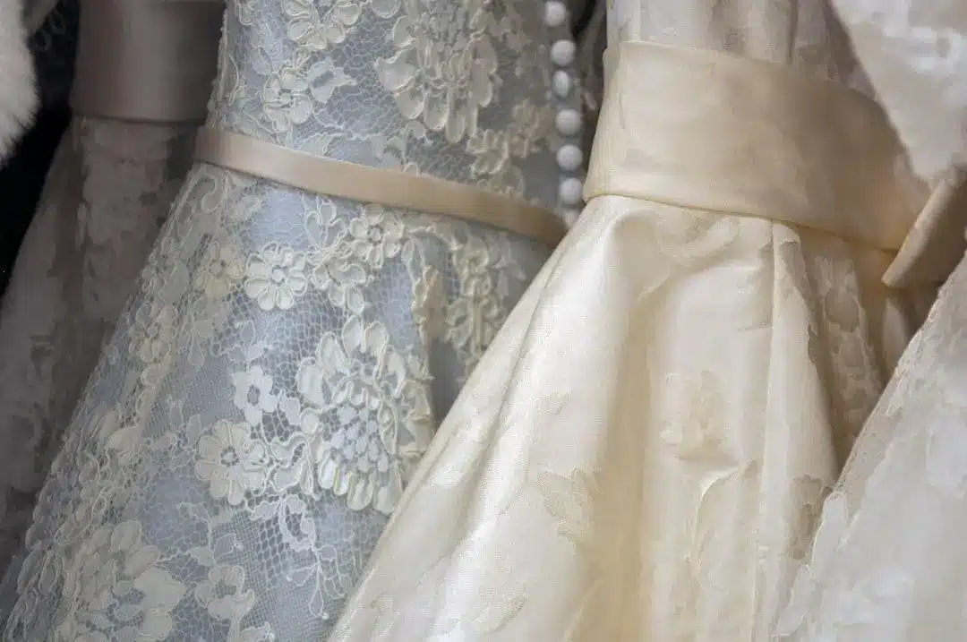 Close-up of detailed lace and satin wedding dresses with floral patterns and button accents