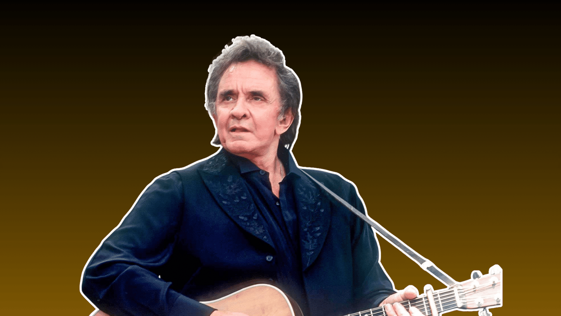 older male musician holding an acoustic guitar while wearing a dark suit against a brown background