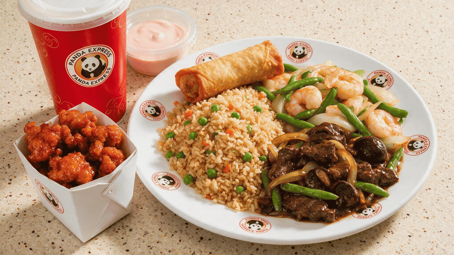 panda Express meal with fried rice, shrimp and vegetables, beef, spring roll, orange chicken, dipping sauce, and a drink.