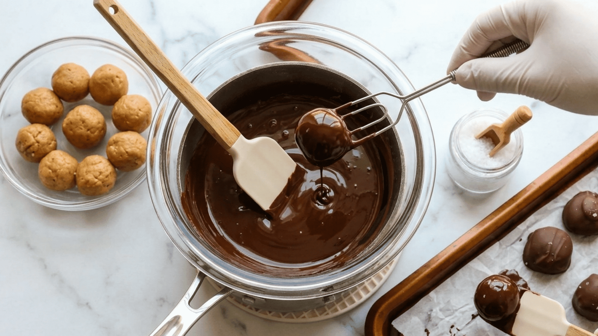 peanut butter balls being dipped in melted chocolate and placed on a parchment lined tray
