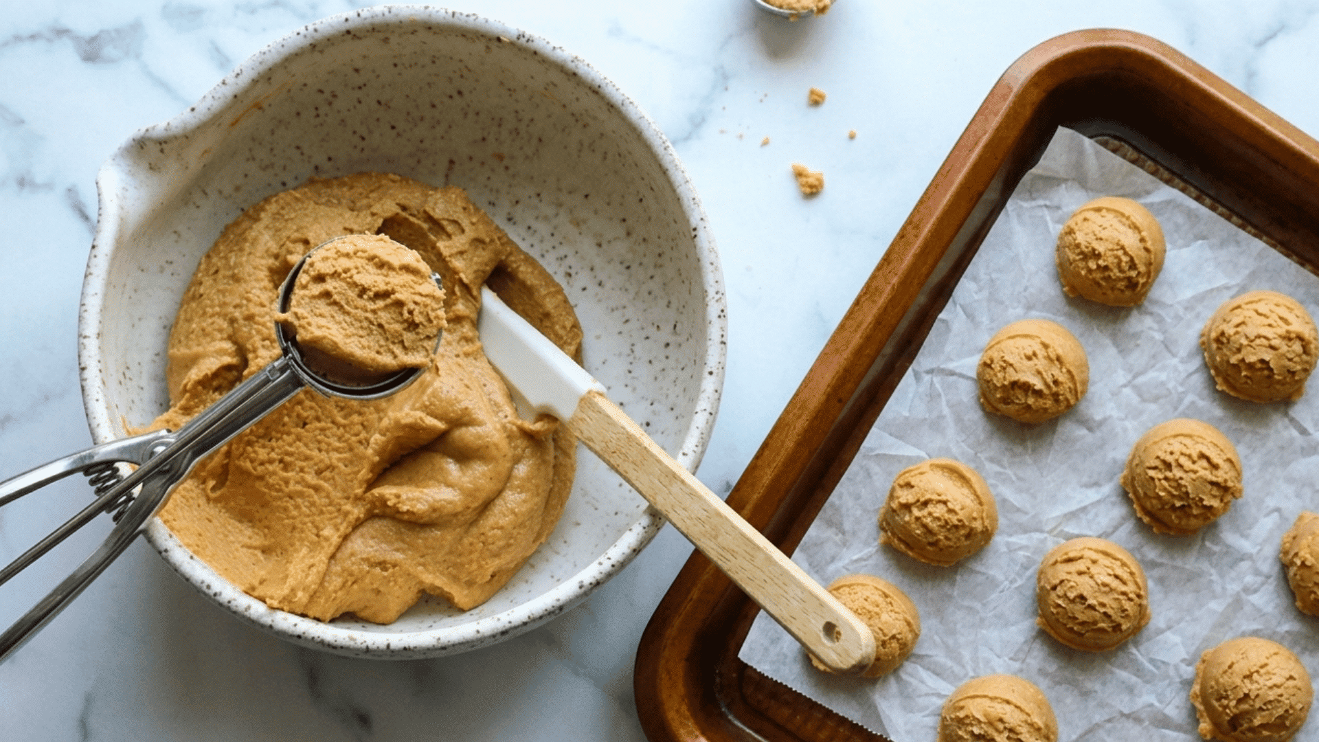 peanut butter mixture being scooped and shaped into small balls on a parchment lined baking tray
