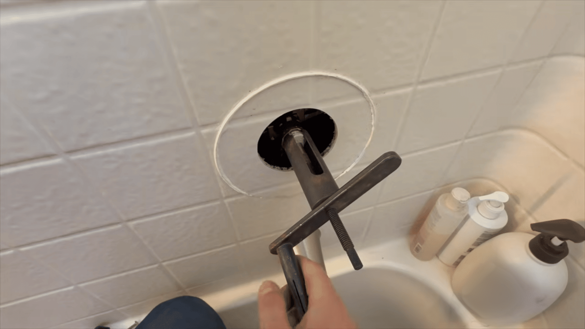 person using metal cartridge puller tool on shower valve in tub area
