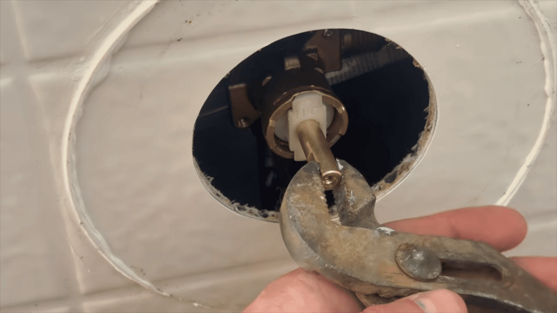pliers gripping and pulling out brass stem of new shower cartridge