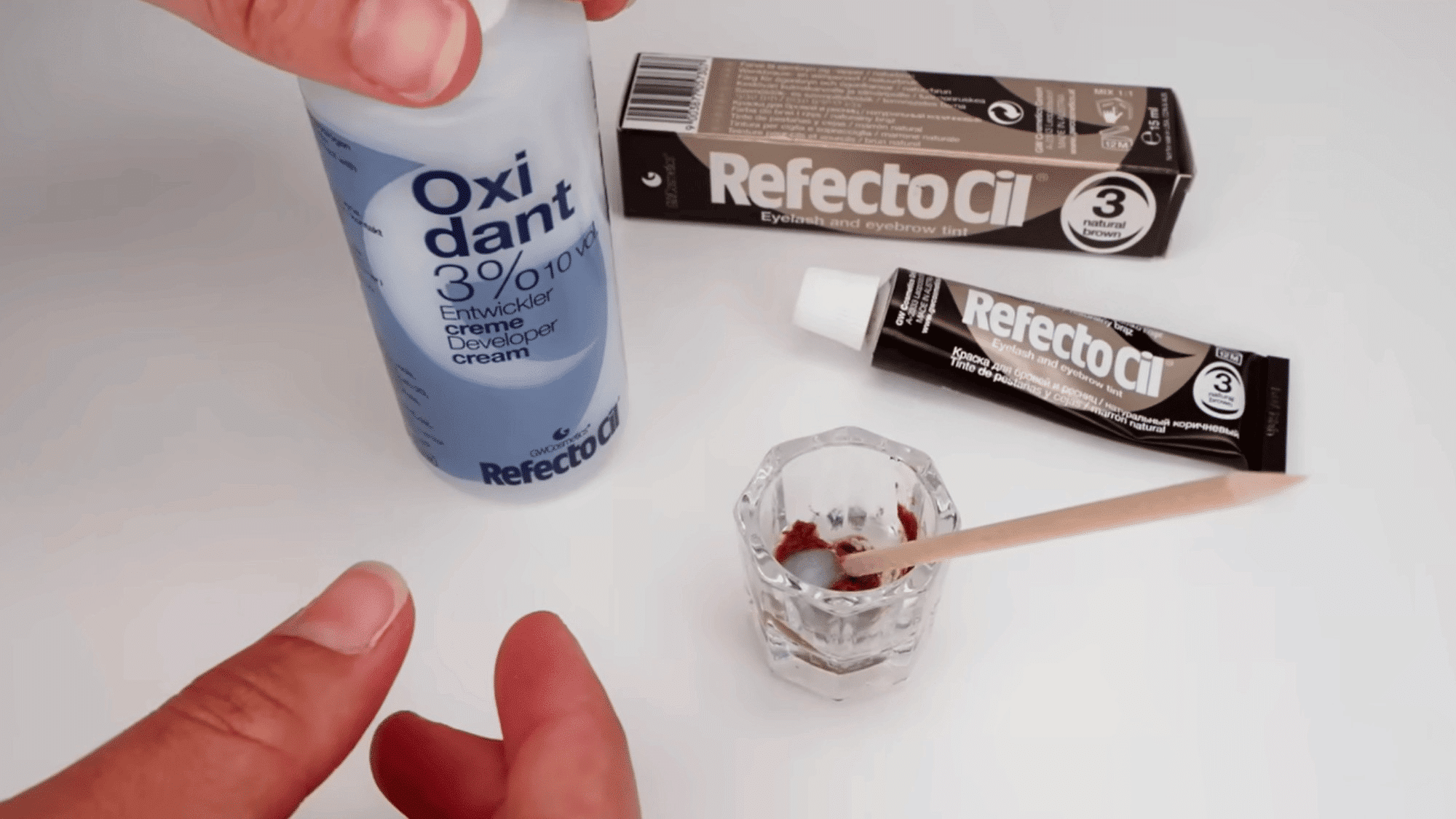 refectocil eyebrow tint and developer cream being mixed in a small glass dish with a wooden applicator
