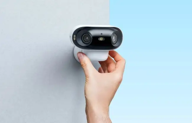 Hand mounting a small white and black security camera on a light-colored wall