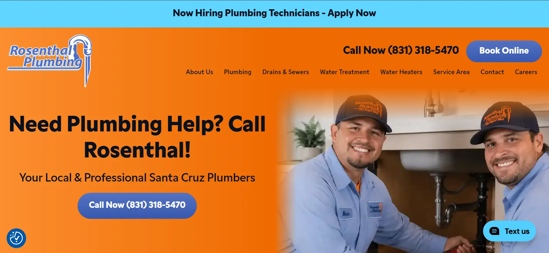 Two plumbers in blue uniforms smiling under a kitchen sink with orange background