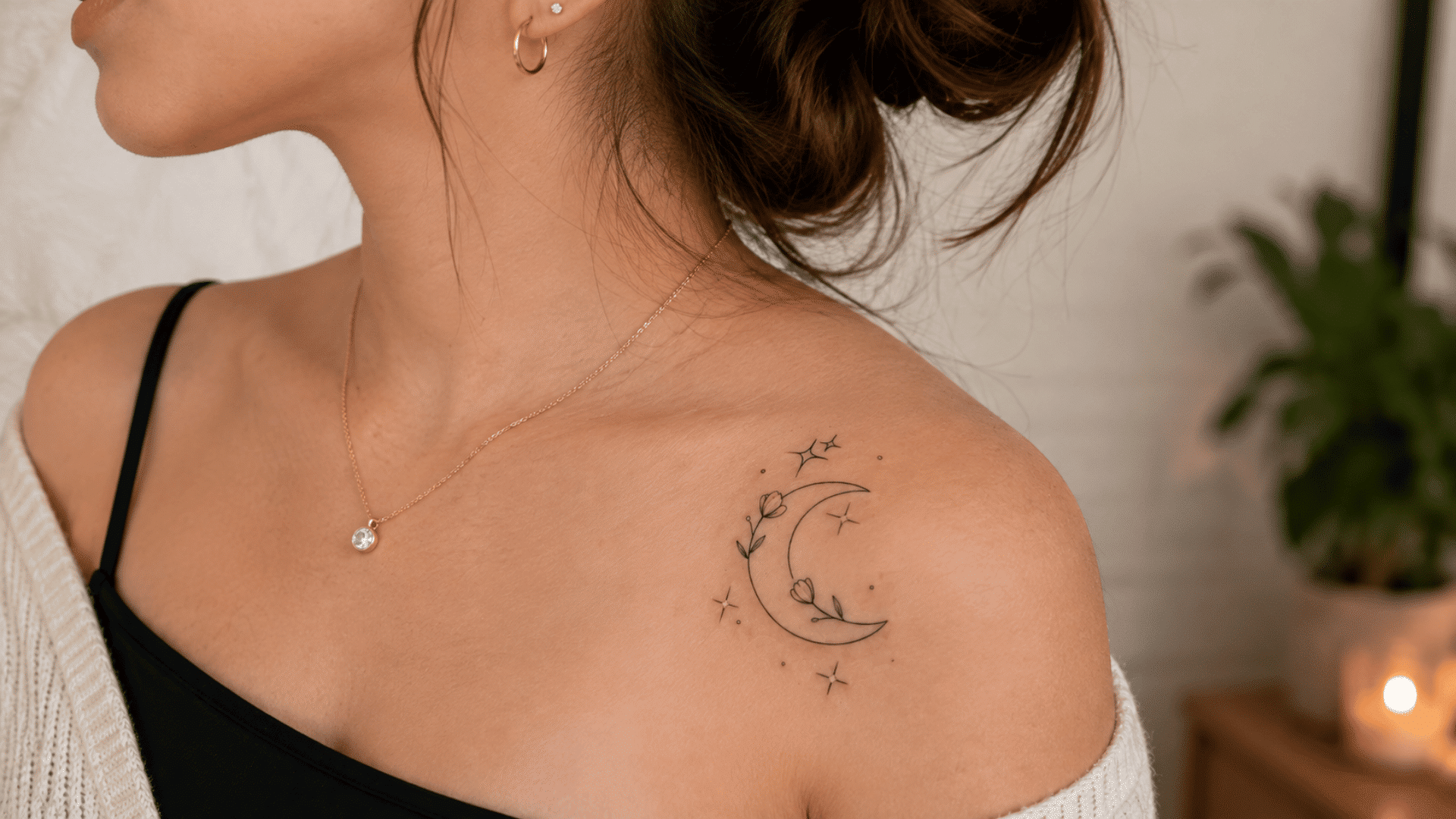 small crescent moon and floral tattoo on a woman’s shoulder with delicate star details.
