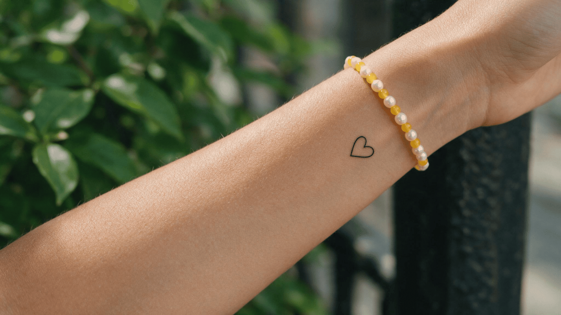 small heart tattoo on the inner wrist beside a white and yellow beaded bracelet.
