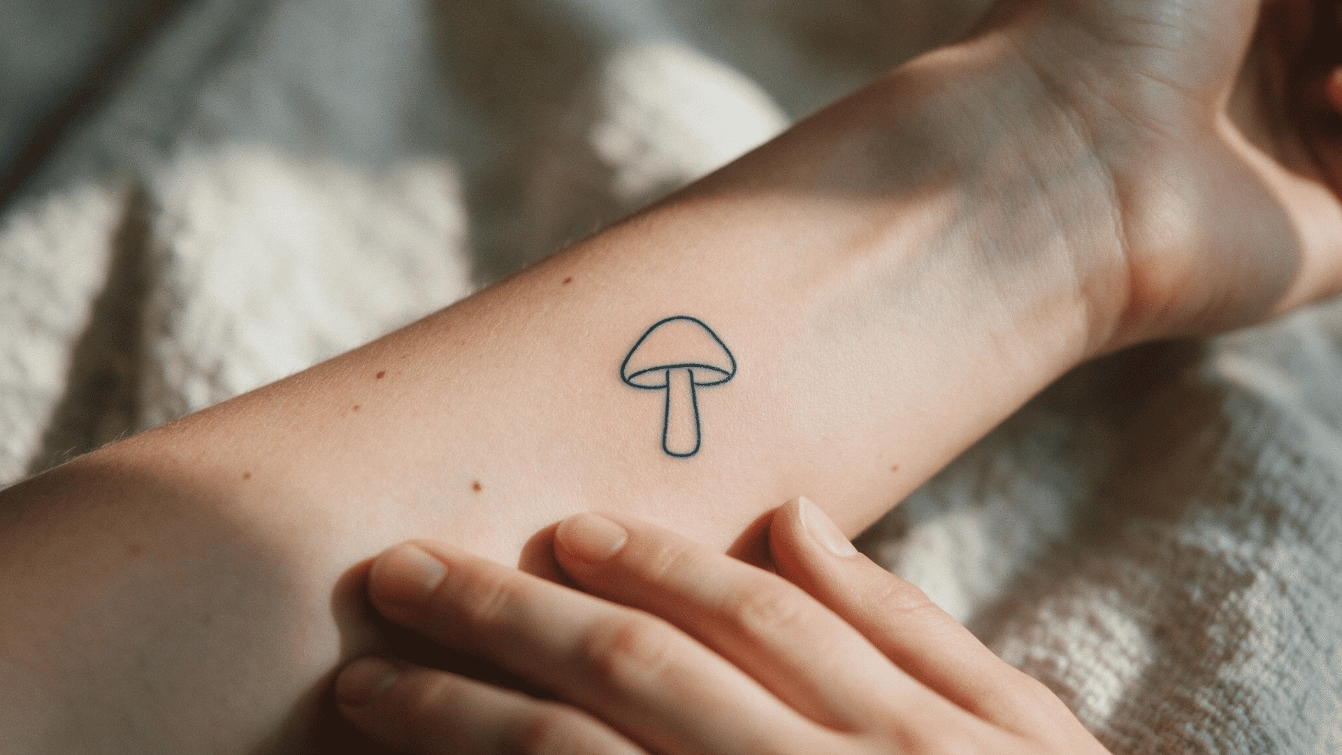 small minimalist mushroom outline tattoo on the inner forearm, shown in warm natural light.